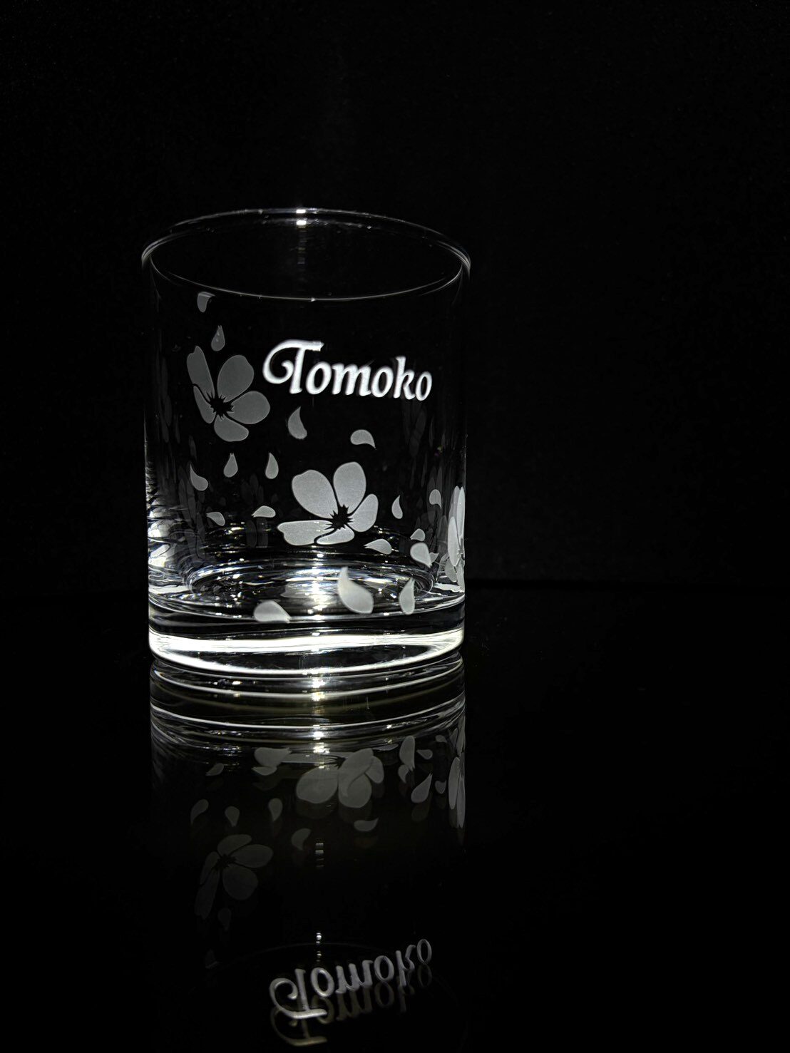 桜の花びらが舞うデザインと「Tomoko」の名入れが施されたロックグラスの写真