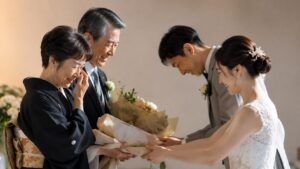 結婚披露宴で、新郎新婦がご両親へ花束と記念品を手渡している様子です。お母様は感動して涙を拭い、お父様は笑顔で見守っています。家族への感謝が伝わる、両親贈呈の場面